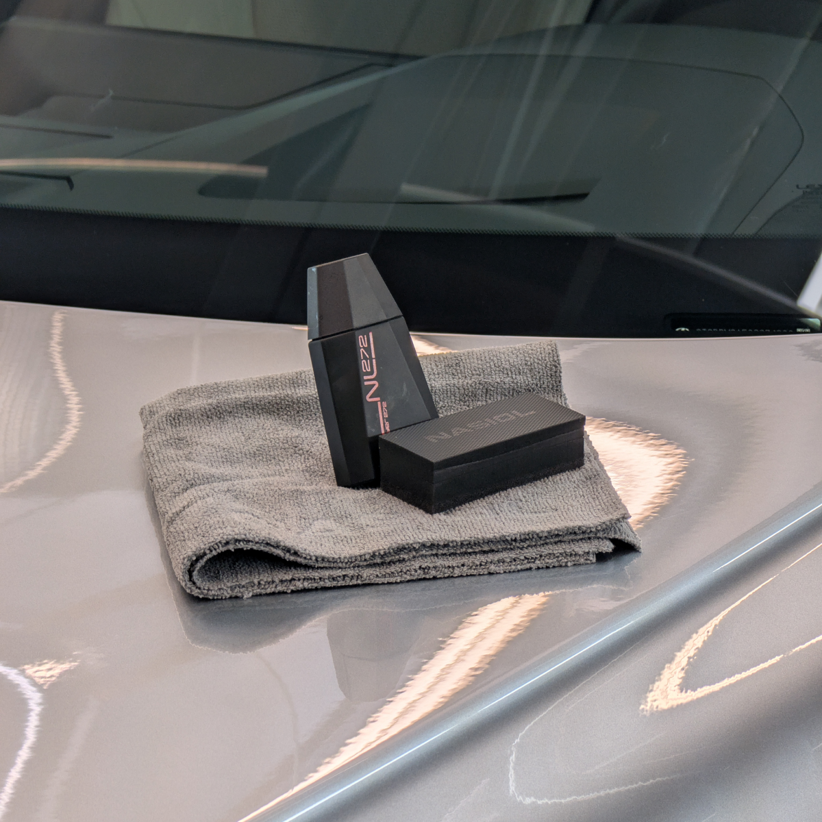 Car detailing kit with product bottle, applicator, and cloth on car hood.