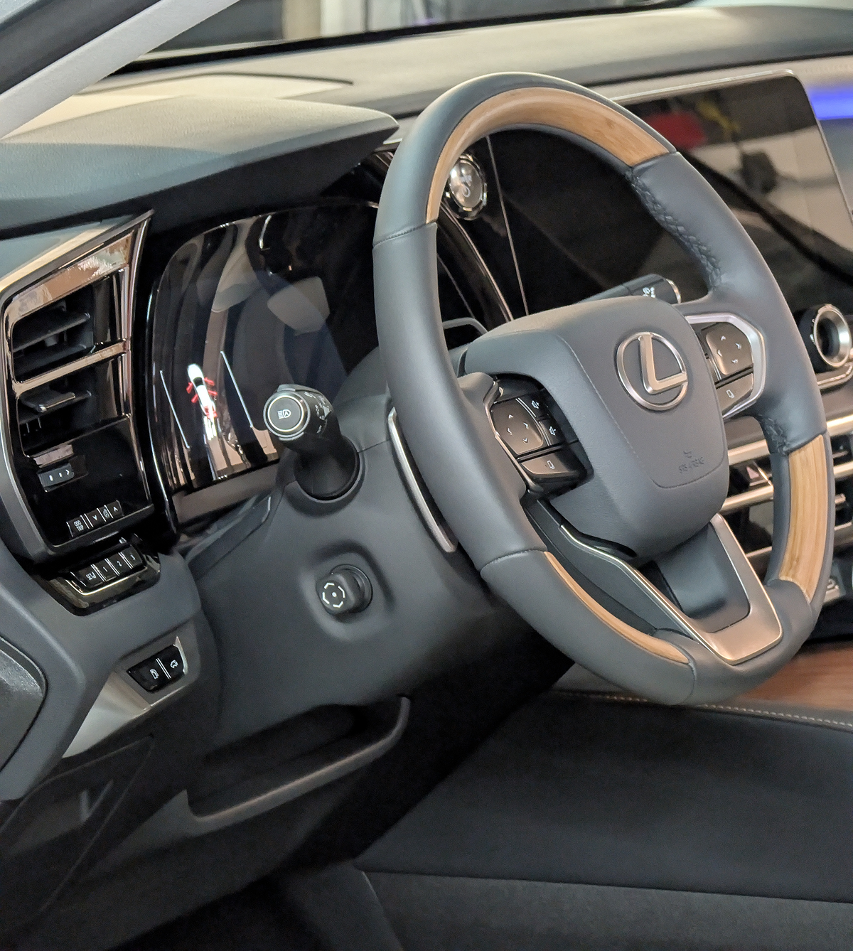 Interior car shot: Gray leather steering wheel with wood accents, Lexus logo, dashboard.