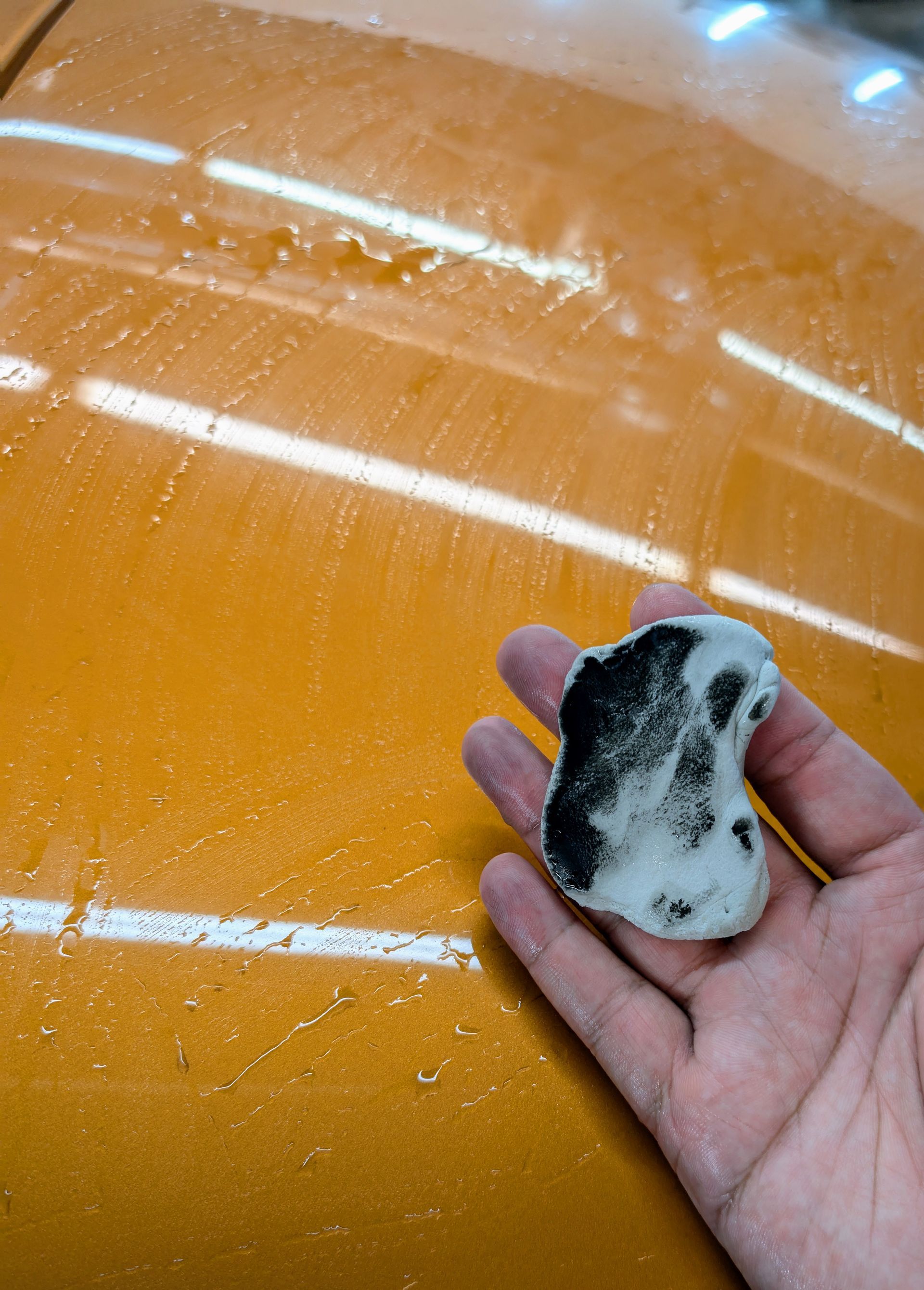 Person scrubbing a black car floor mat with soap and a brush on a concrete floor.