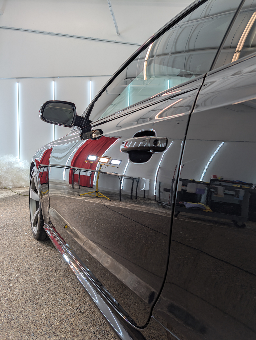 Black car in a well-lit space, reflecting the interior, with its side visible.