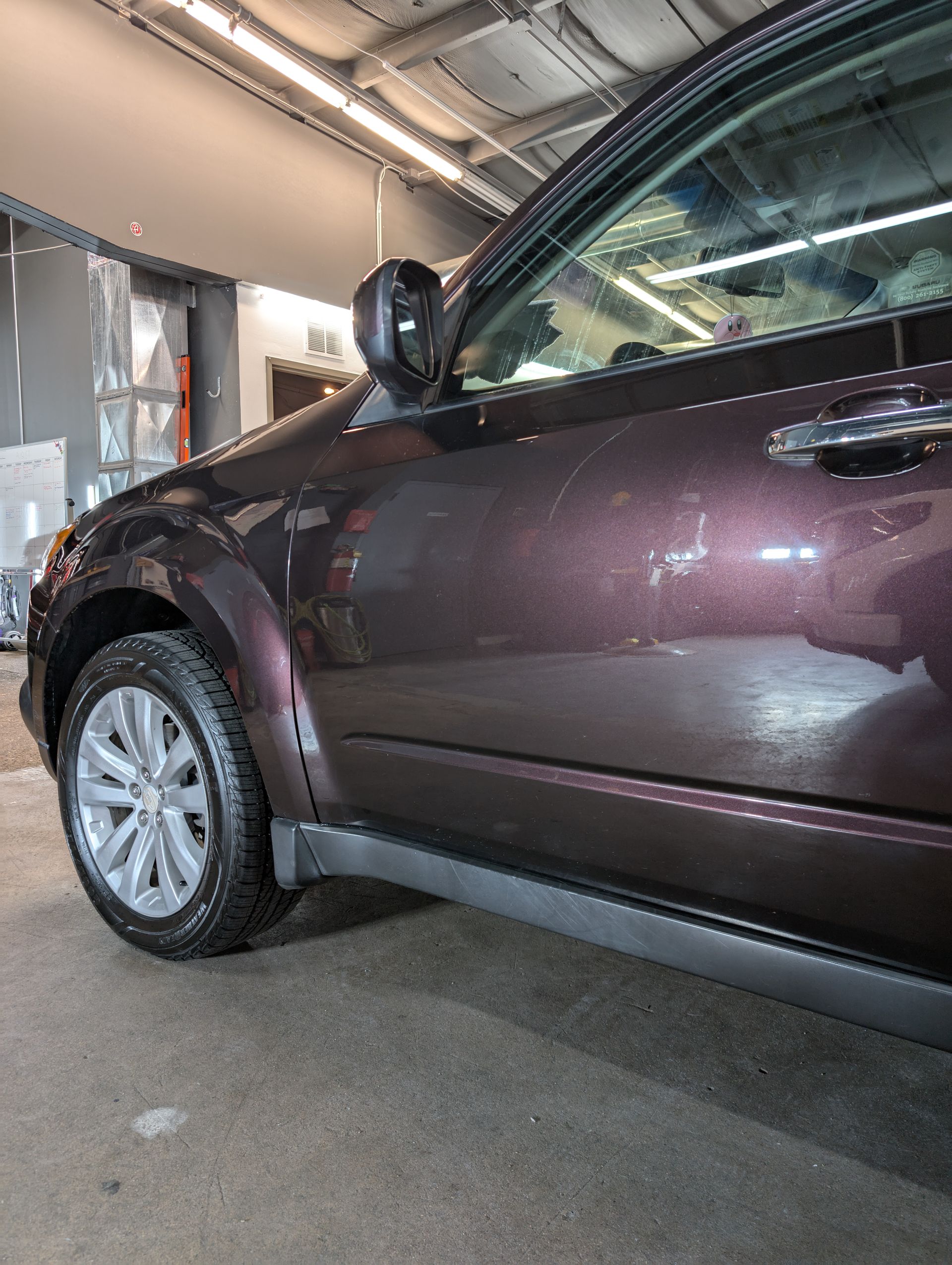 Dark maroon SUV, front side view, parked inside, with silver wheel.