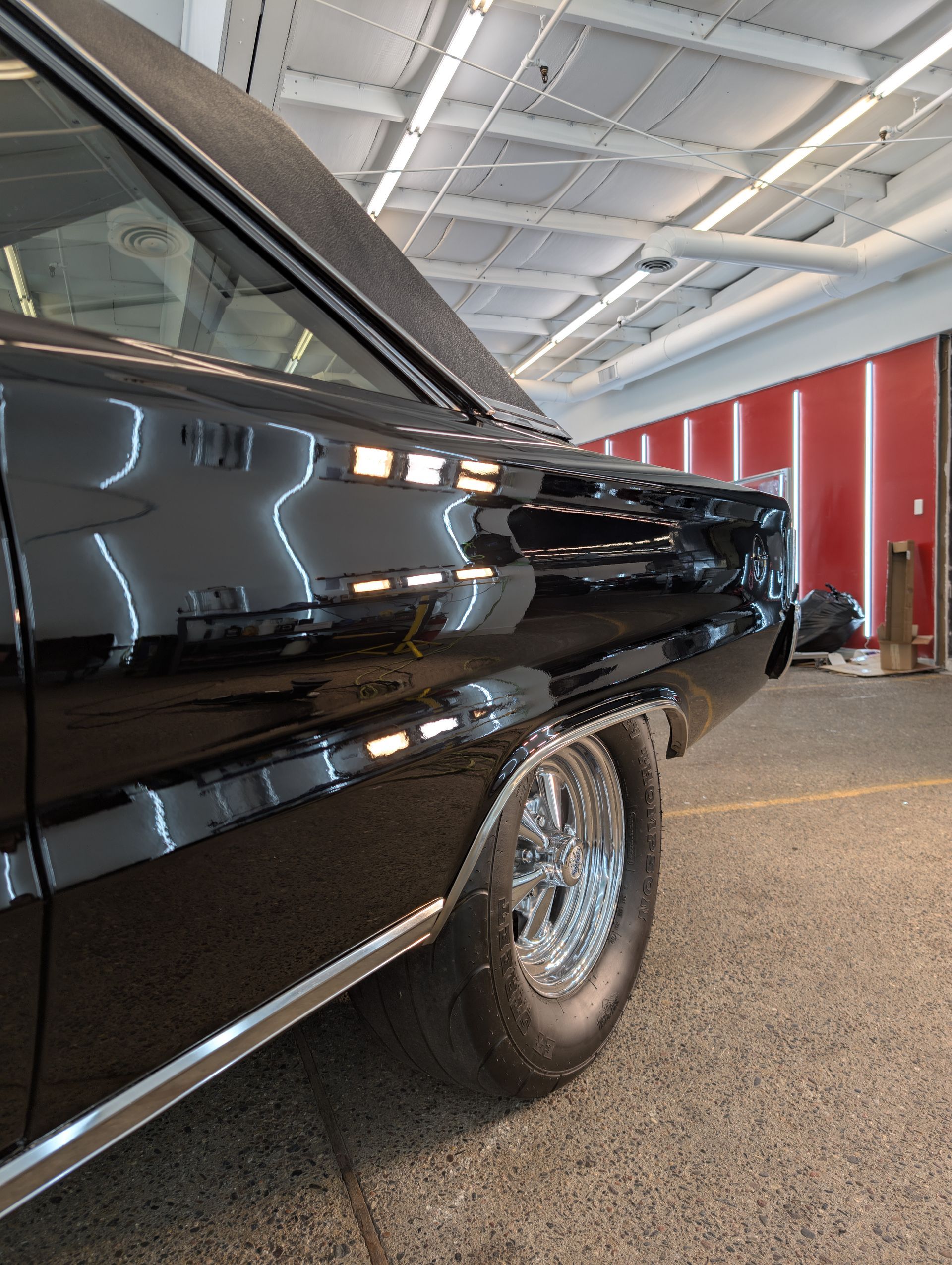 Black classic car, shiny chrome wheels, in an indoor garage setting.