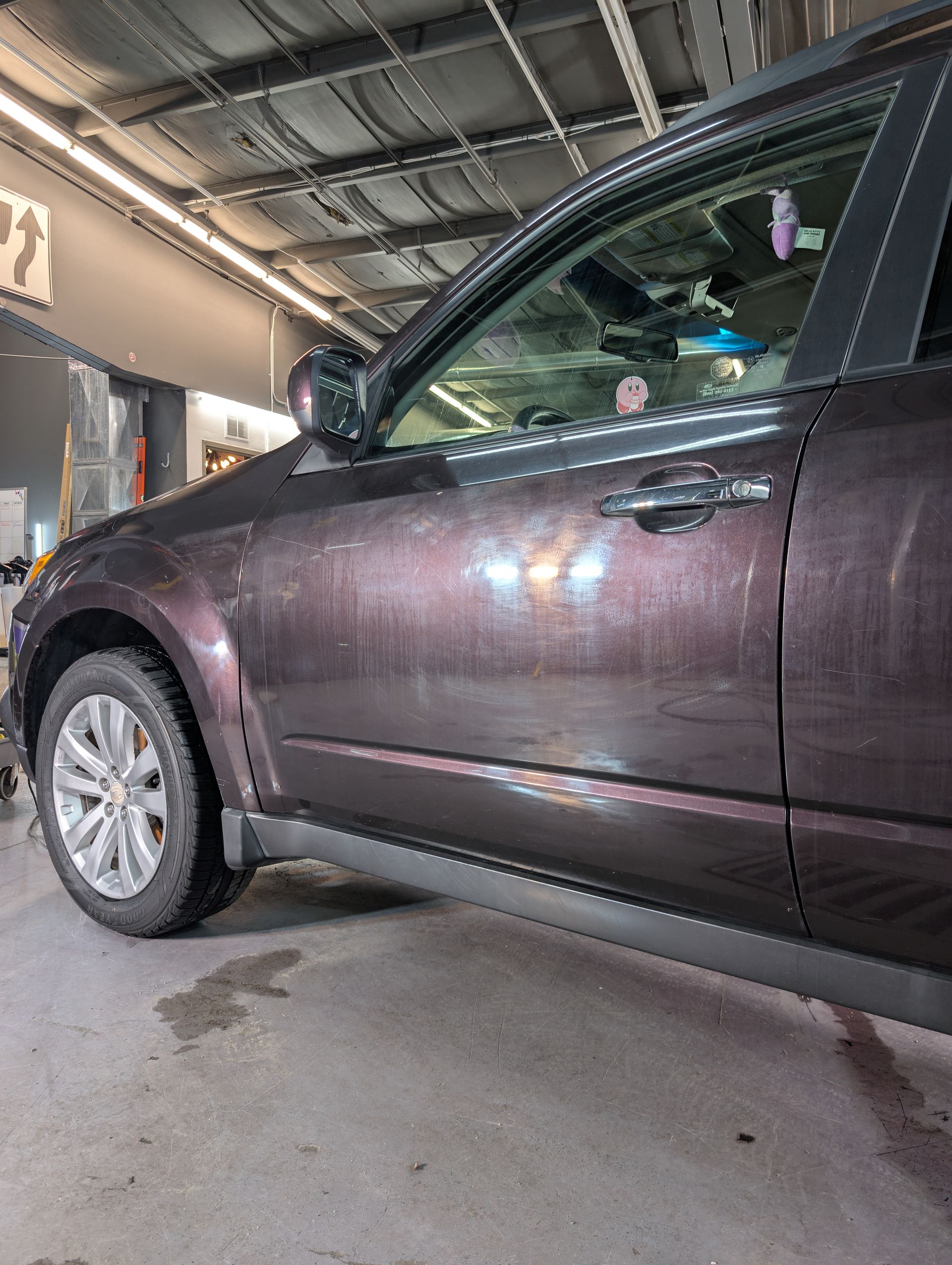 Side view of a dark purple SUV parked indoors, showing the front tire and door details.