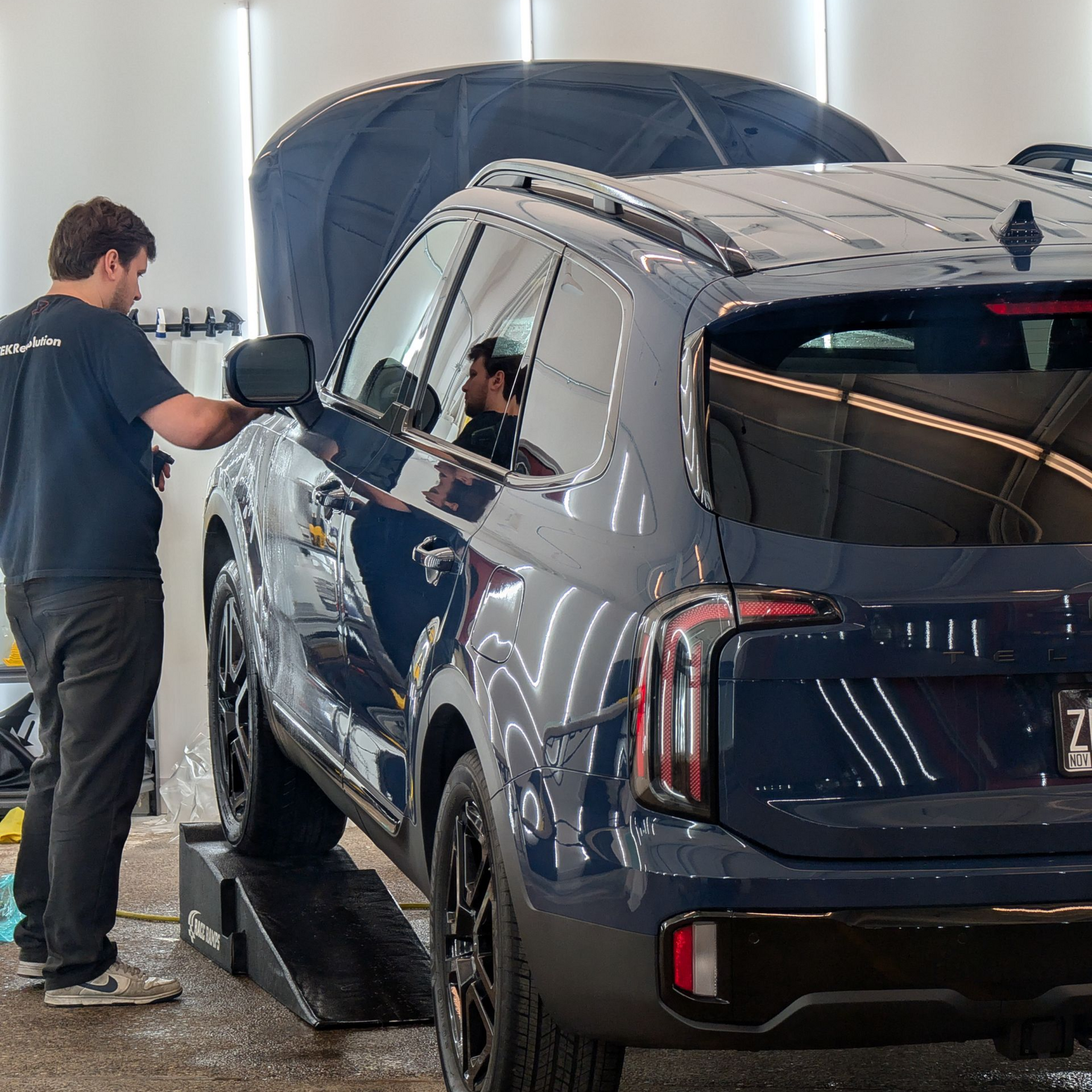 Person applying clear protective film to the front of a red car.