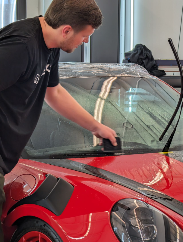 Person applying window tint to a blue car, using hands to smooth out the film and bubbles.