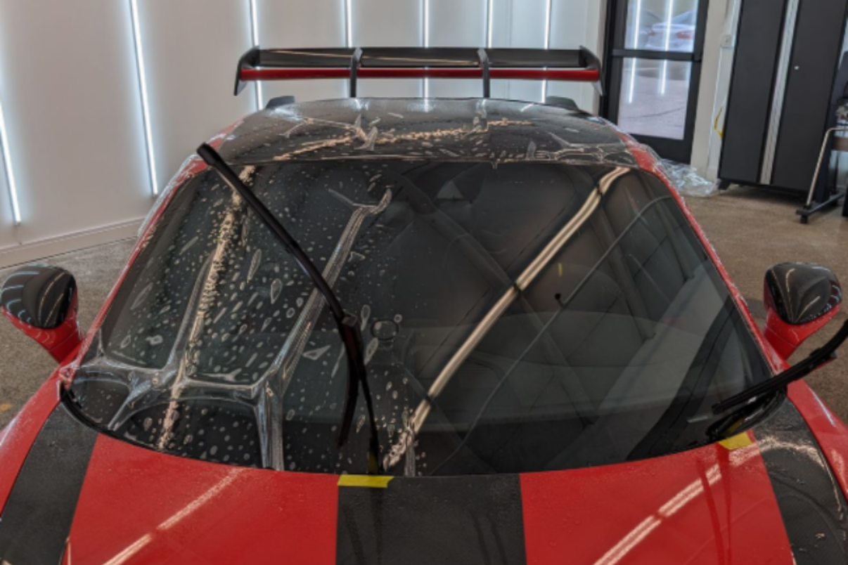 Red sports car with black stripes and a wet windshield.