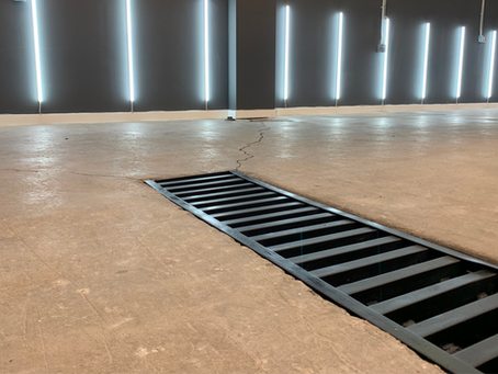 Grayscale photo of an industrial floor with a drain and long lights on the wall.