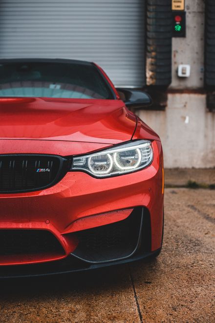 Red BMW M4 sports car parked near a garage in the rain.