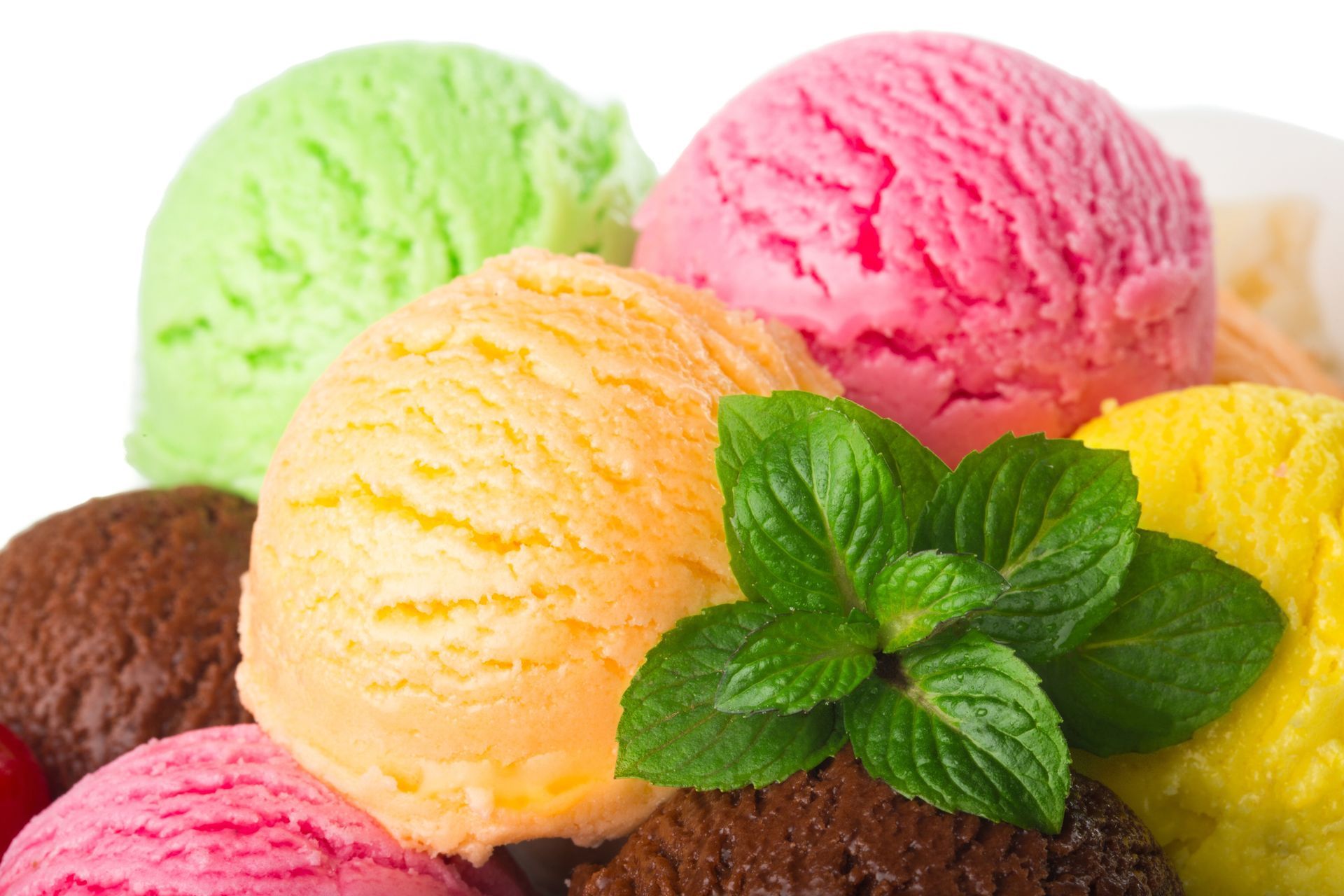 There are many different flavors of ice cream on a plate with mint leaves.