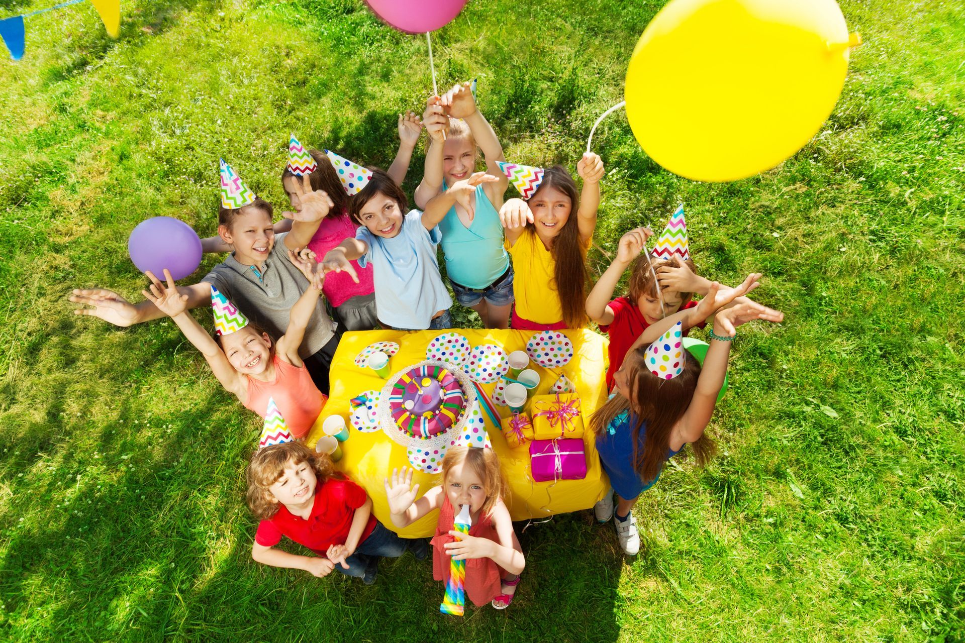 A group of children are sitting around a table with balloons and gifts at a birthday party.