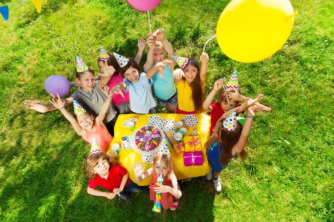 A group of children are sitting around a table with balloons and gifts at a birthday party.