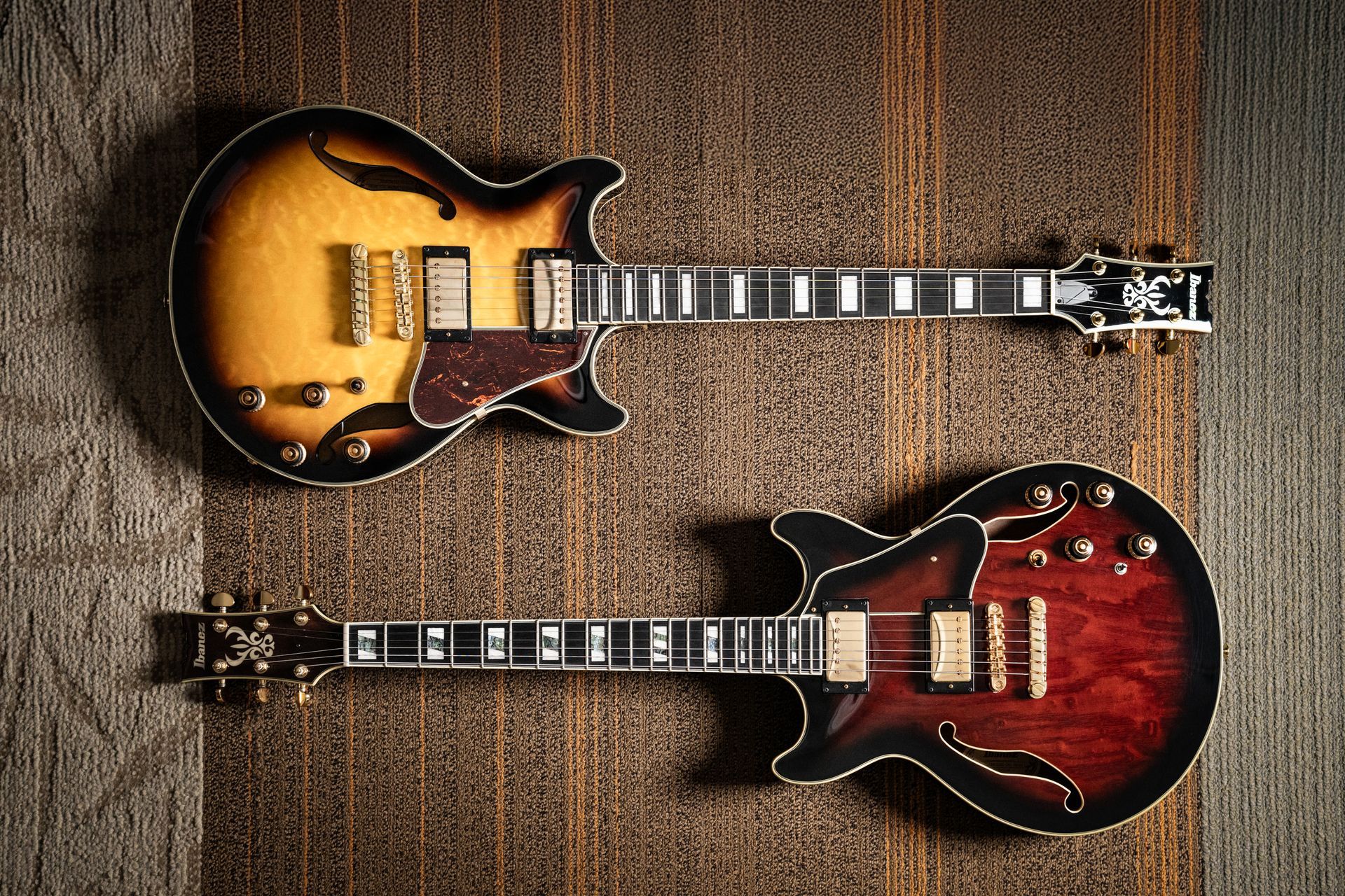 Two electric guitars with sunburst and red finishes on a wooden surface.