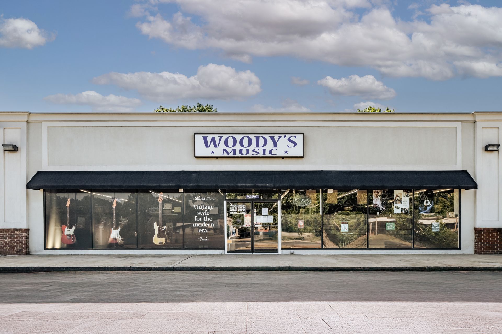 Woody's Music storefront with sign, windows, and awning on a sunny day.