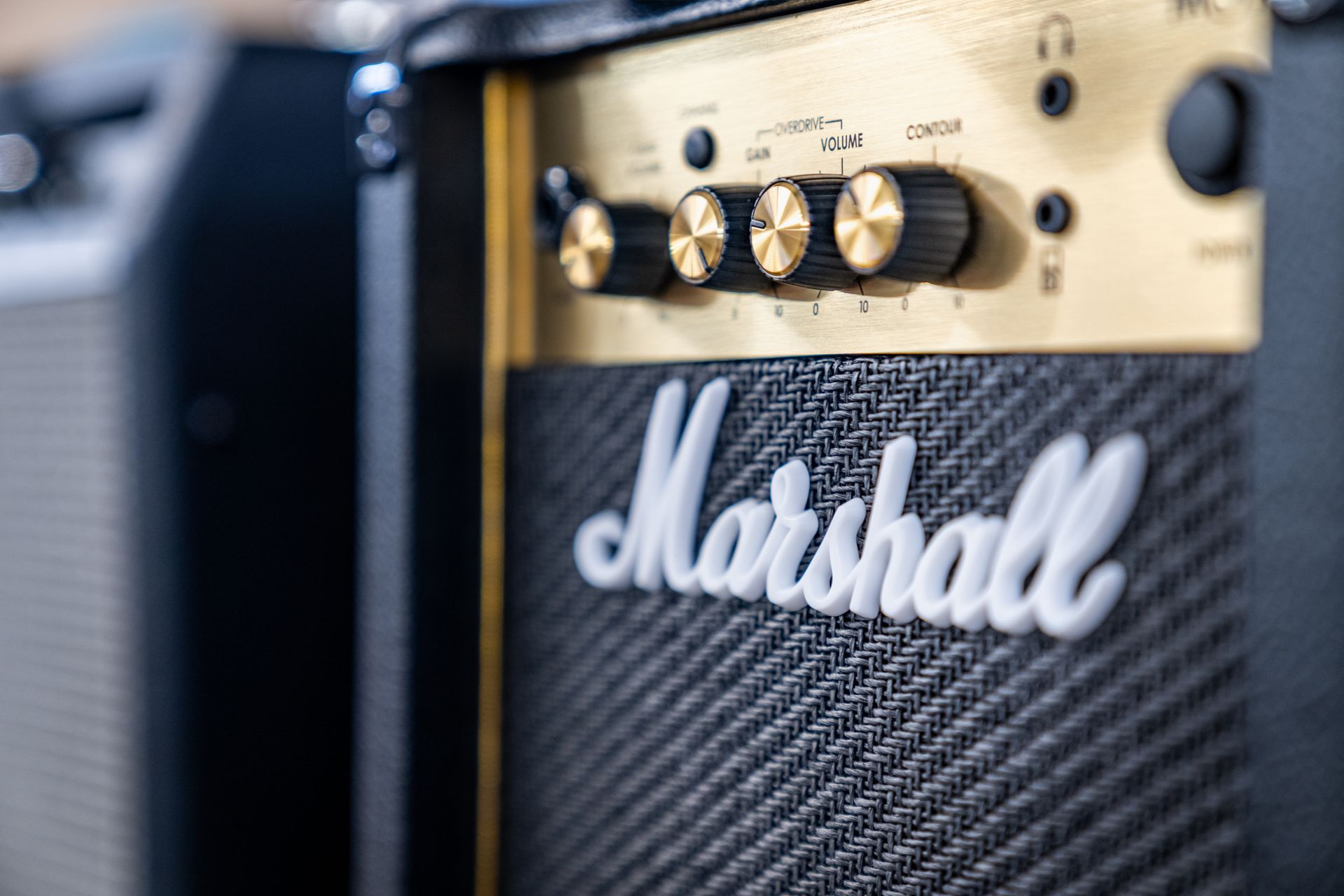 Close-up of a Marshall amplifier, gold control panel, black speaker grill, white Marshall logo.