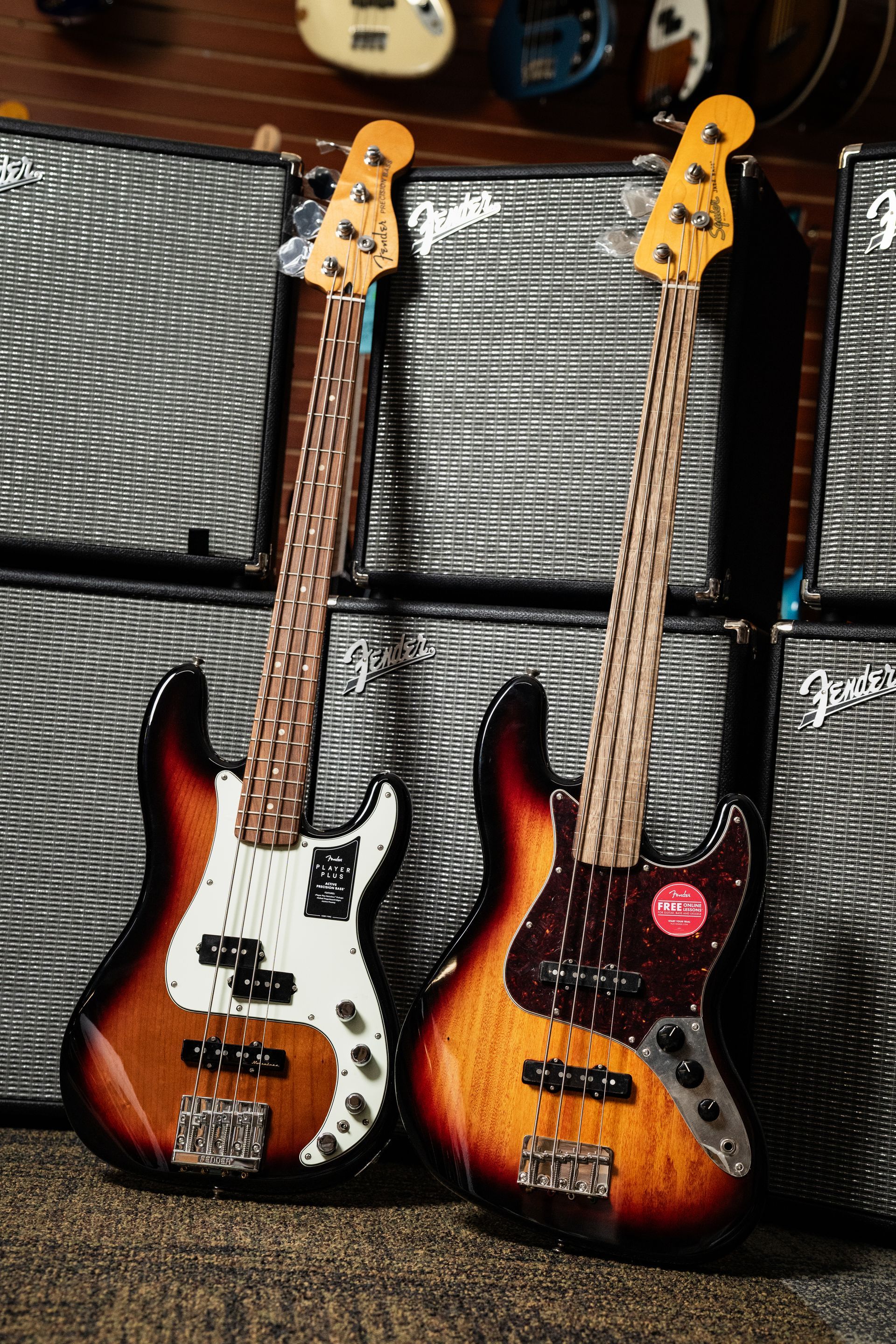 Two sunburst bass guitars leaning against silver amplifiers.