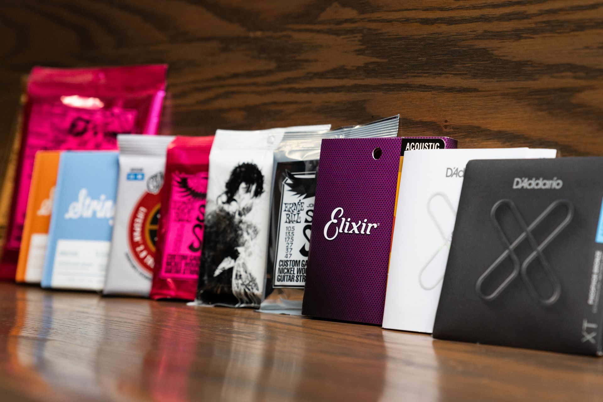 Bags of guitar strings in various colors and brands lined up on a wooden surface.