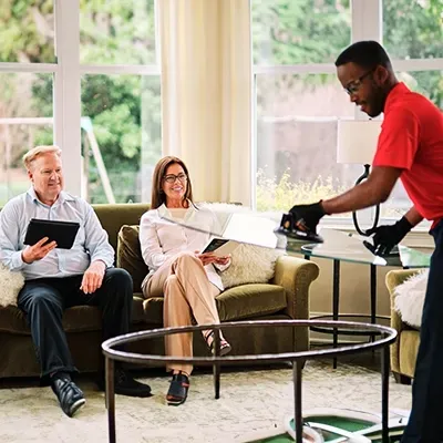 Man in red shirt installing glass table top for seated couple in living room.