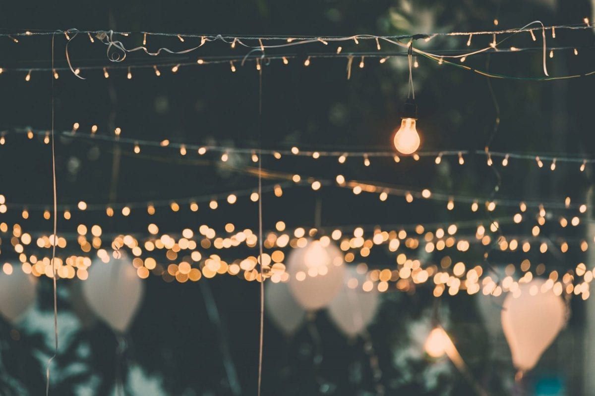 Strings of warm white lights and white balloons against a dark background, suggesting a nighttime outdoor celebration.