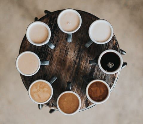 Coffee mugs arranged in a circle, displaying various shades of coffee with milk, on a wooden surface.