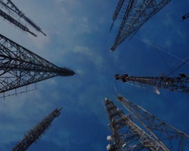 Low-angle view of multiple communication towers against a deep blue sky.