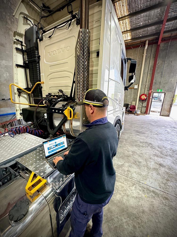 A Man is Doing Diagnostics on a Truck in a Garage While Using a Laptop — Inline Truck and Plant in Tuggerah, NSW