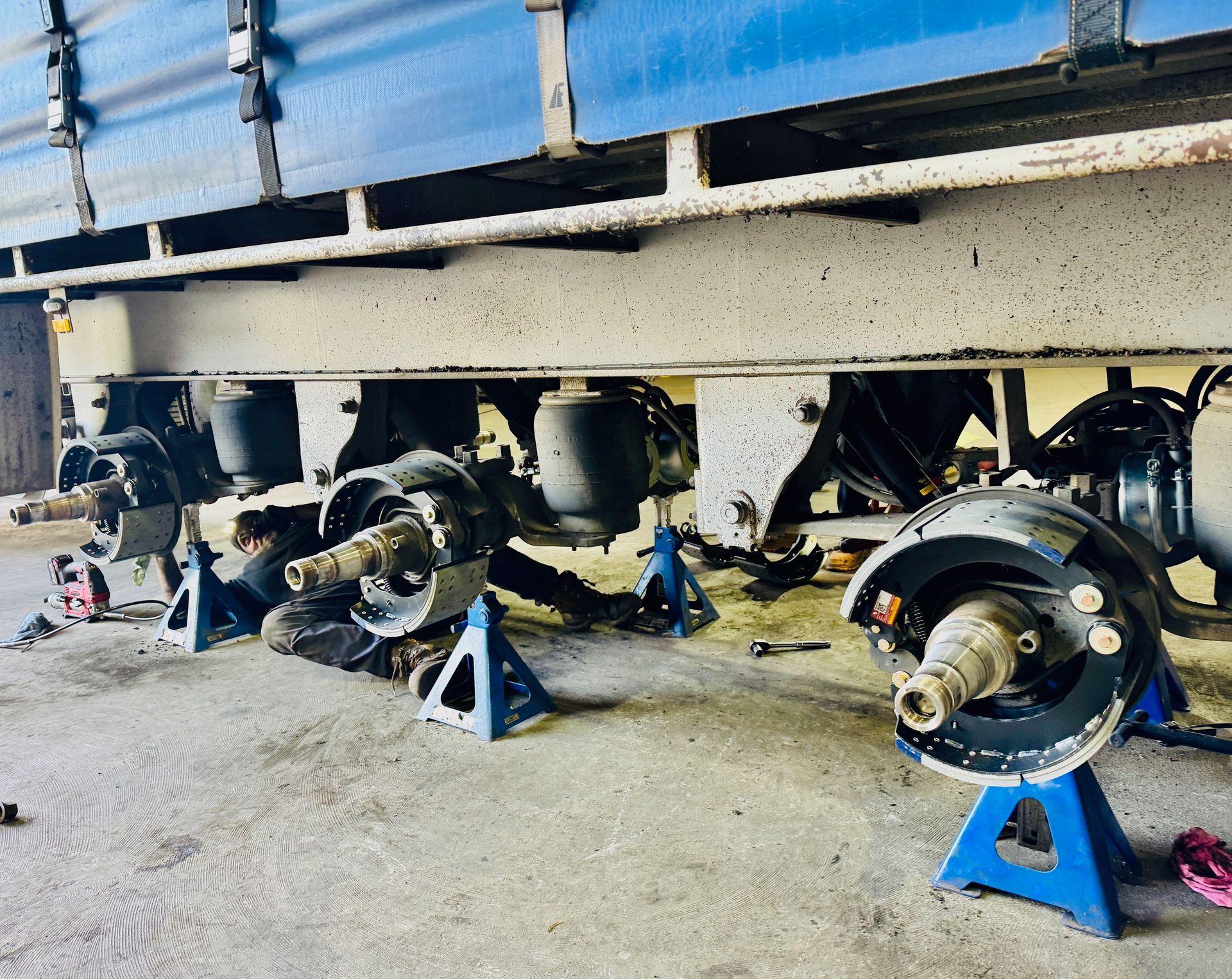 A Man is working on the frame of a suspended blue truck— Inline Truck and Plant in Tuggerah, NSW