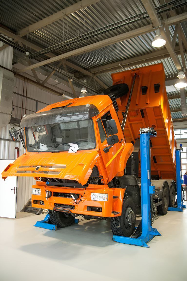 An Orange Dump Truck is on a Lift in a Garage — Inline Truck and Plant in Tuggerah, NSW