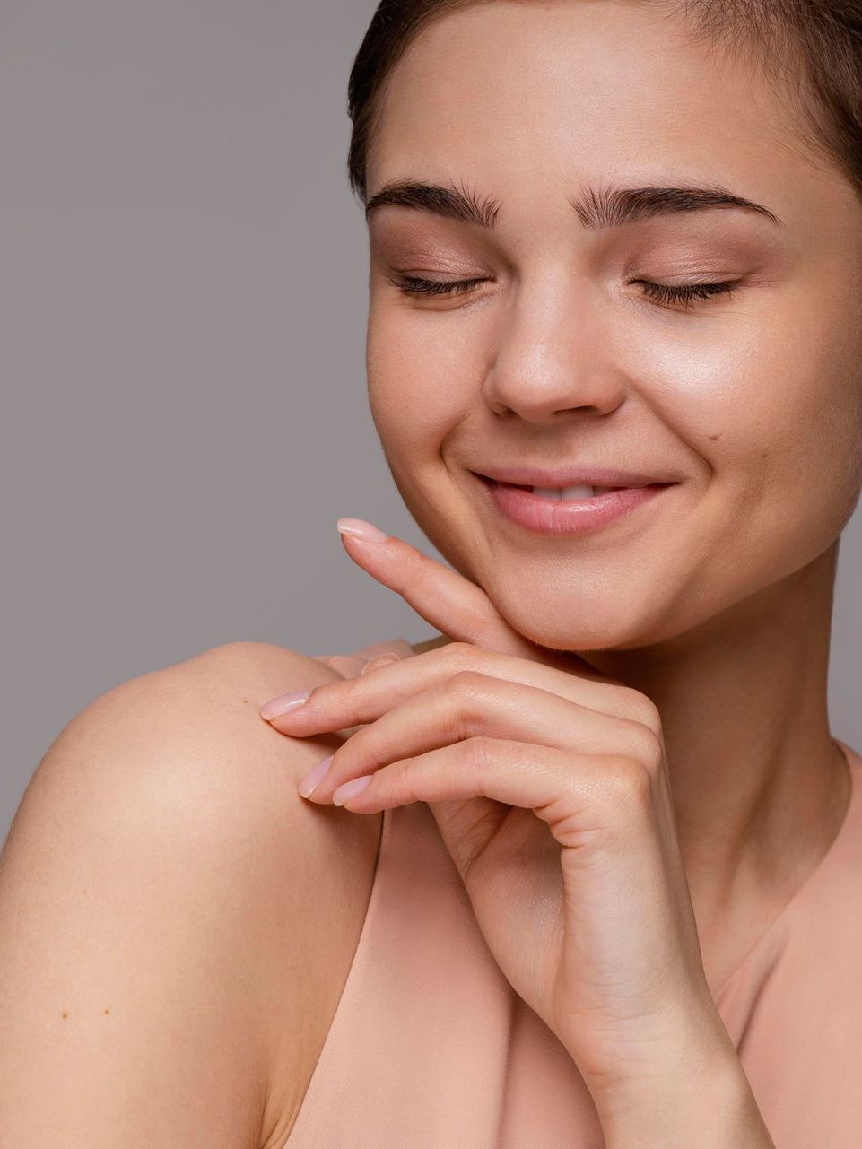 A woman is touching her face with her hand and smiling.