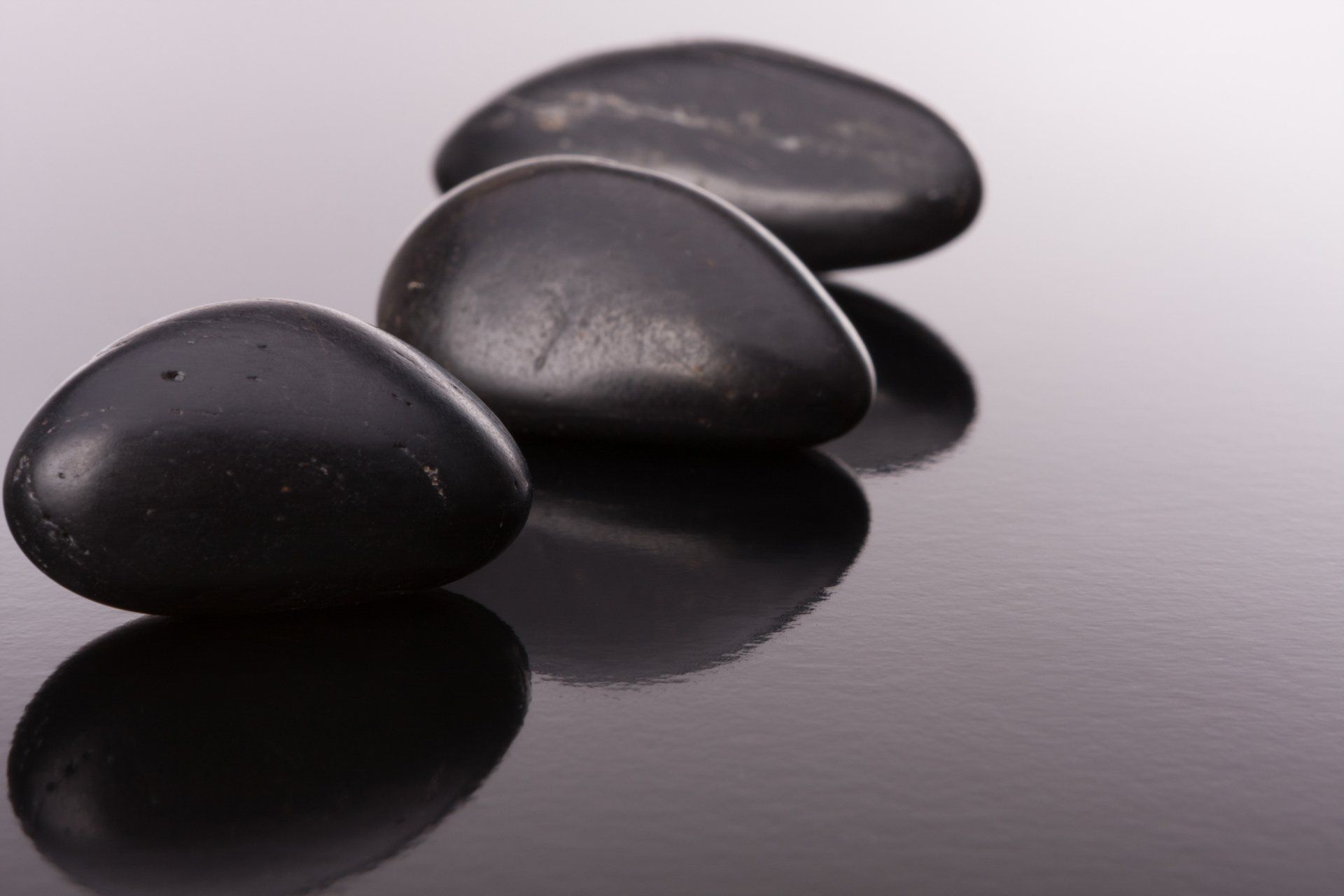 Three black rocks are lined up in a row on a black surface.