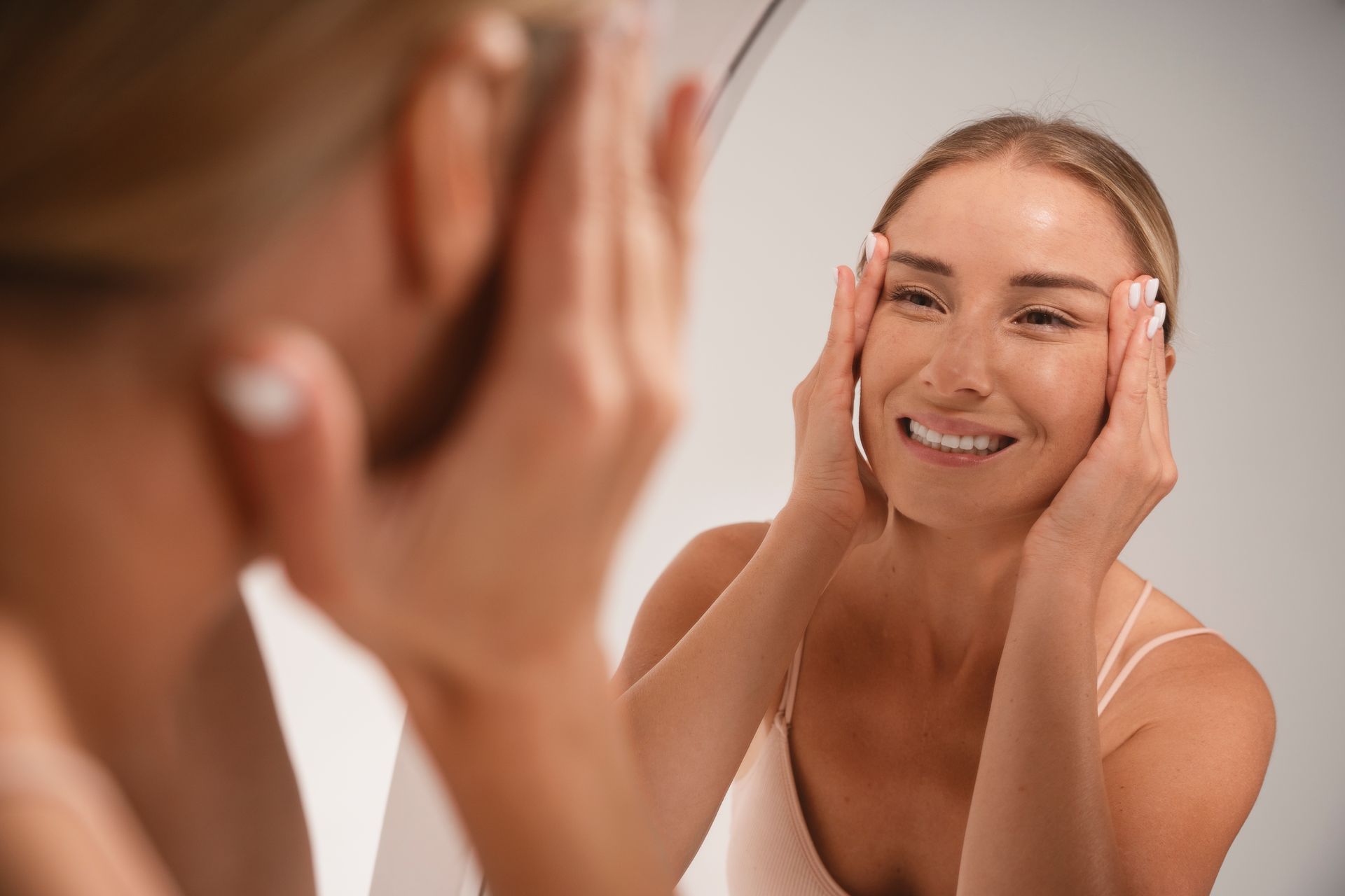 A woman is smiling while looking at her face in a mirror.
