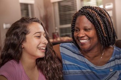 A mother and daughter are sitting next to each other on a couch and smiling.
