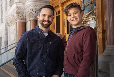 A man and a boy are standing next to each other in front of a building.