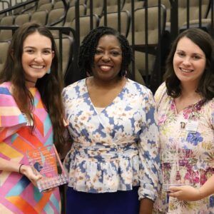 Three women are posing for a picture while one of them is holding a trophy.