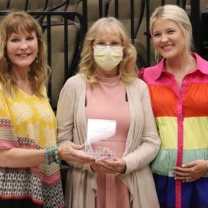 Three women wearing face masks are standing next to each other holding a trophy.