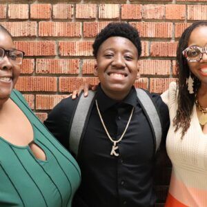Three people are posing for a picture in front of a brick wall.