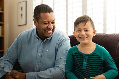 A man and a boy are sitting on a couch and smiling.