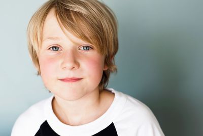 A young boy with blonde hair is wearing a white and black shirt and looking at the camera.