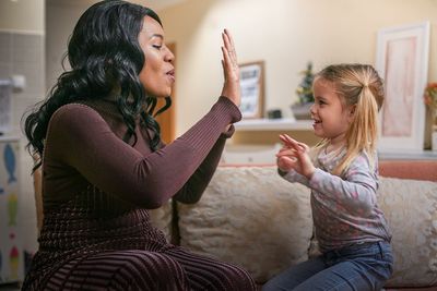A woman and a little girl are sitting on a couch giving each other a high five.