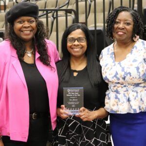 Three women are posing for a picture and one of them is holding a plaque.