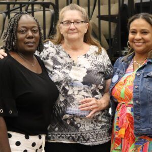 Three women are posing for a picture together in front of a fence.