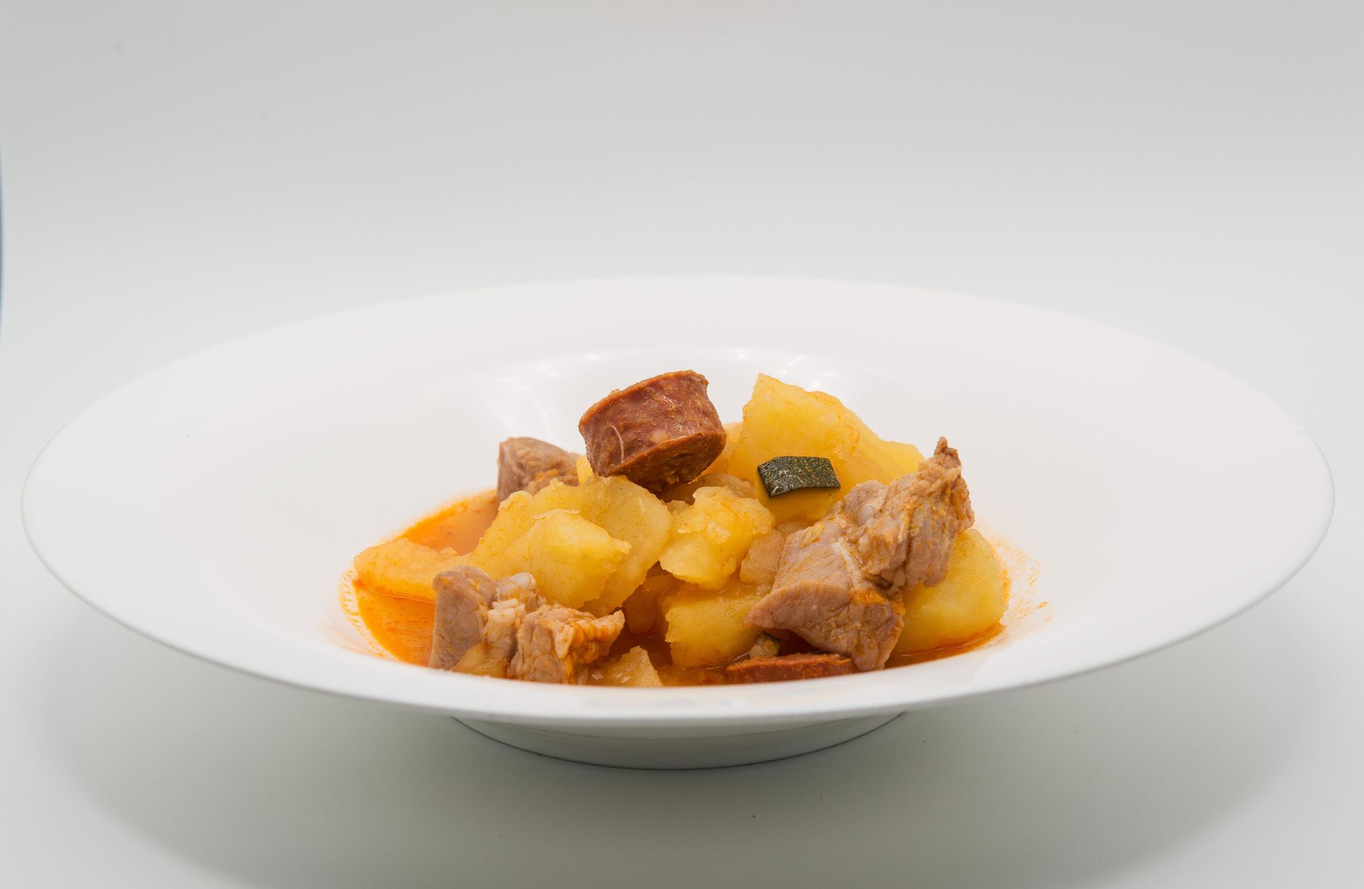 Un plato blanco cubierto con patatas y carne sobre una superficie blanca.