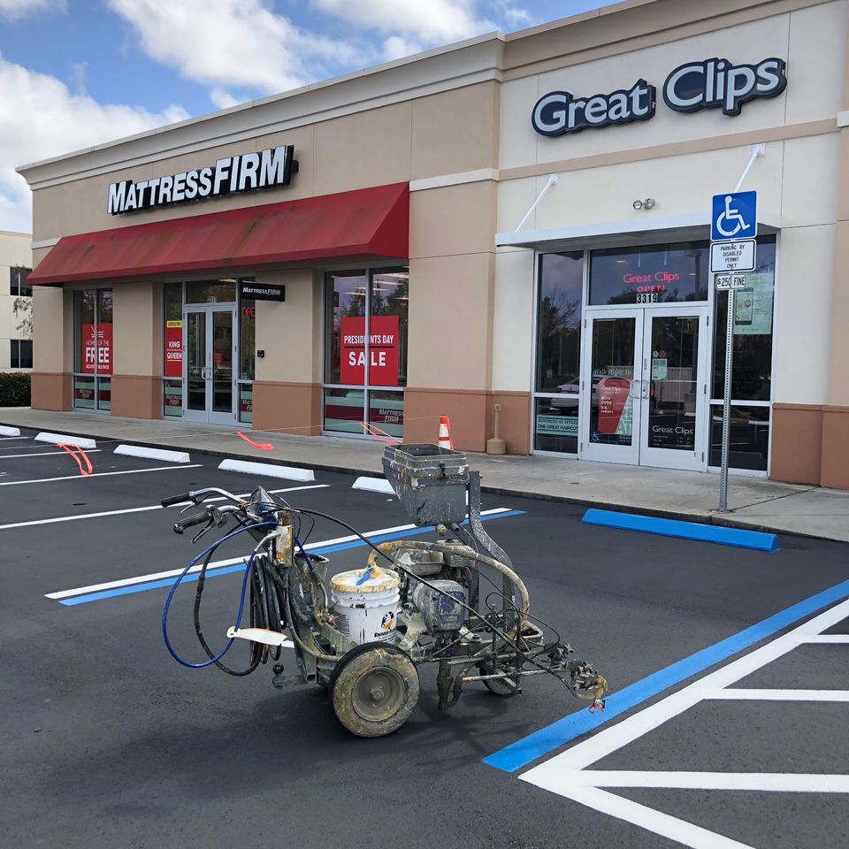 A parking lot being repainted. A striping machine paints blue accessible parking spot lines.