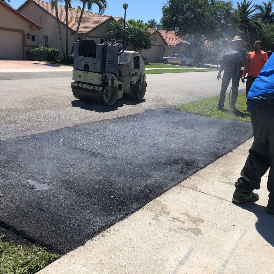 Asphalt paving in residential area, roller compacting fresh blacktop. Workers nearby.
