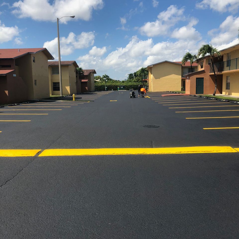 Newly paved parking lot with yellow parking space lines; workers in orange vests.