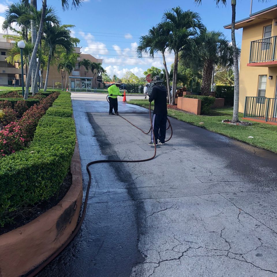 Two people pressure washing an asphalt road, residential setting.