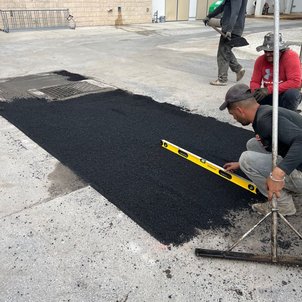 Workers laying asphalt, leveling with a long yellow level, on a concrete surface.