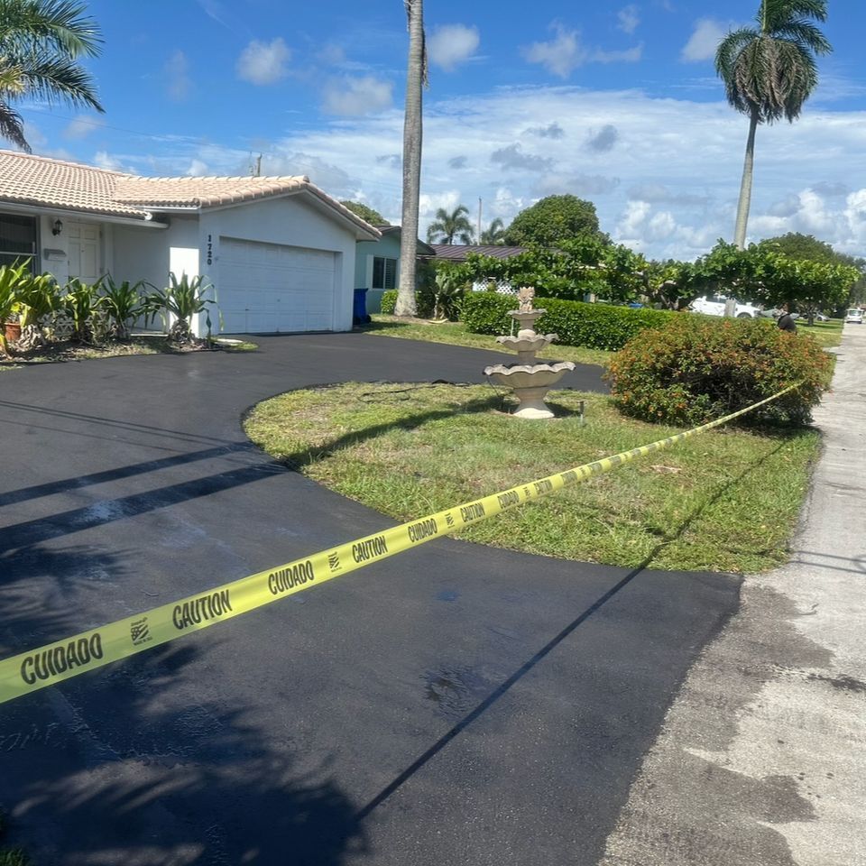 Freshly paved driveway, caution tape in front of a white house with tropical landscaping, sunny day.