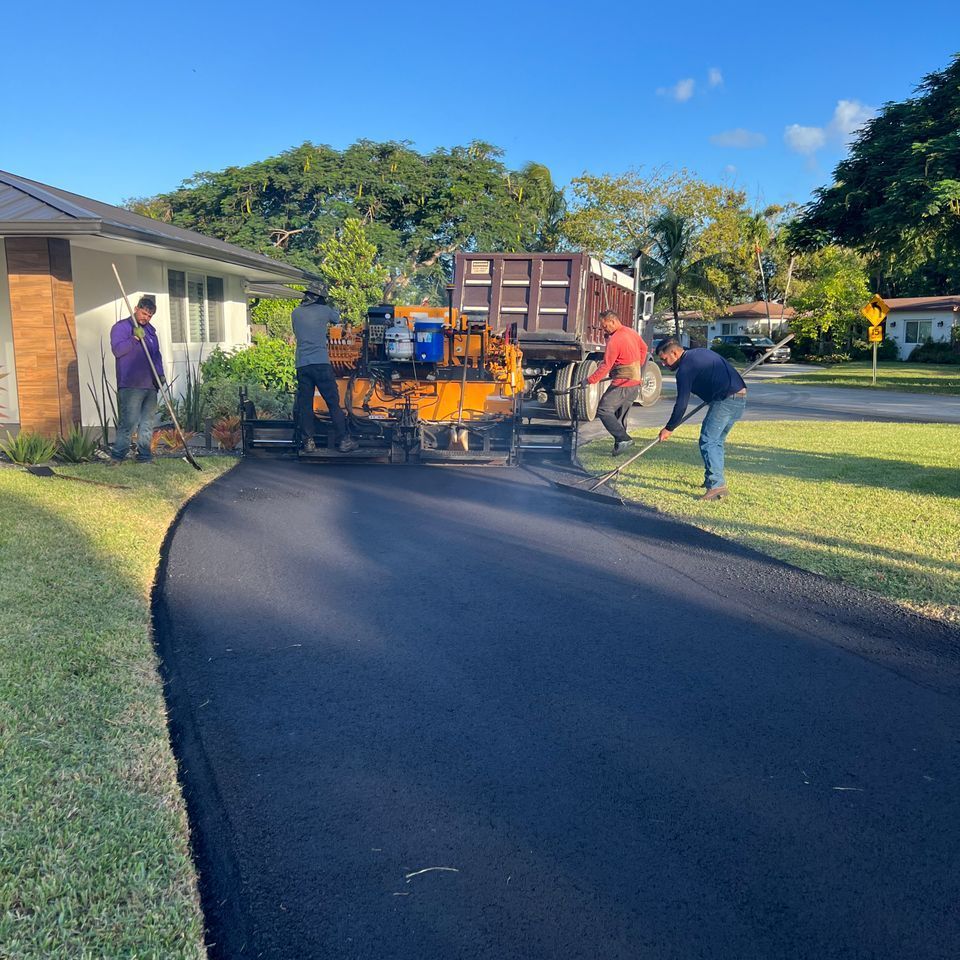 Asphalt paving crew resurfacing a curved driveway in front of a house. Workers use tools, truck in background.