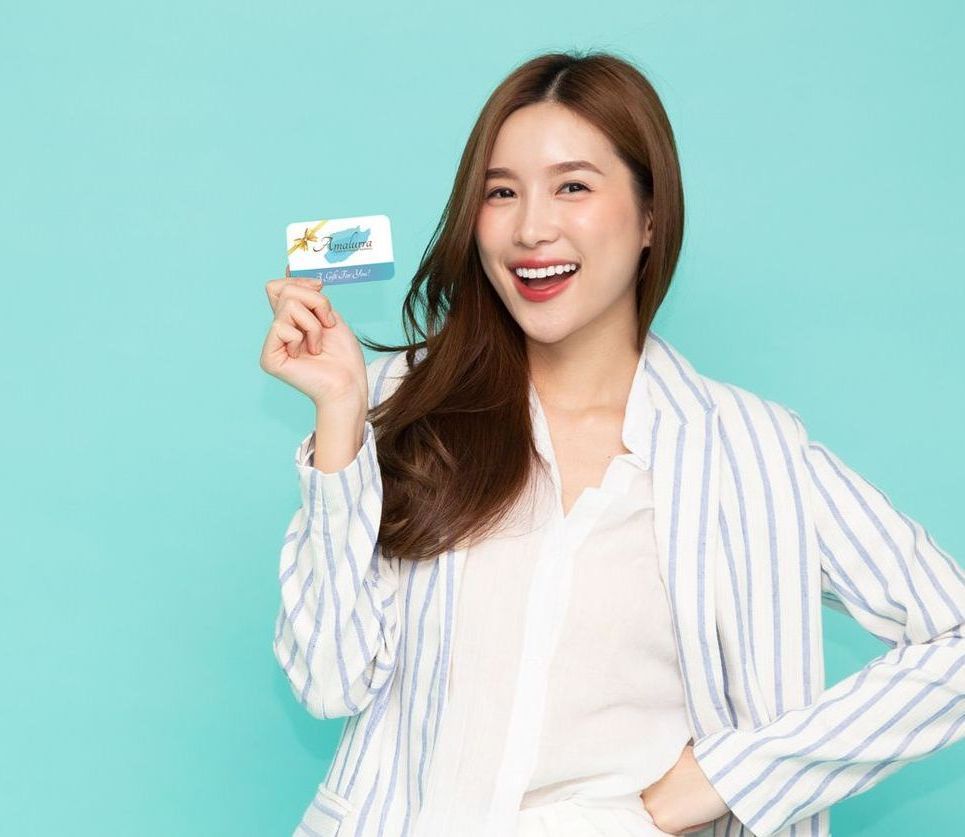 happy young asian woman holding up a gift card from Amalurra Centre for Medical Aesthetics
