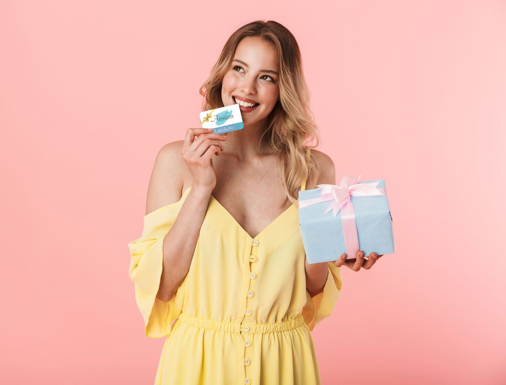 happy young blonde woman holding a gift box and gift card from Amalurra Centre for Medical Aesthetics